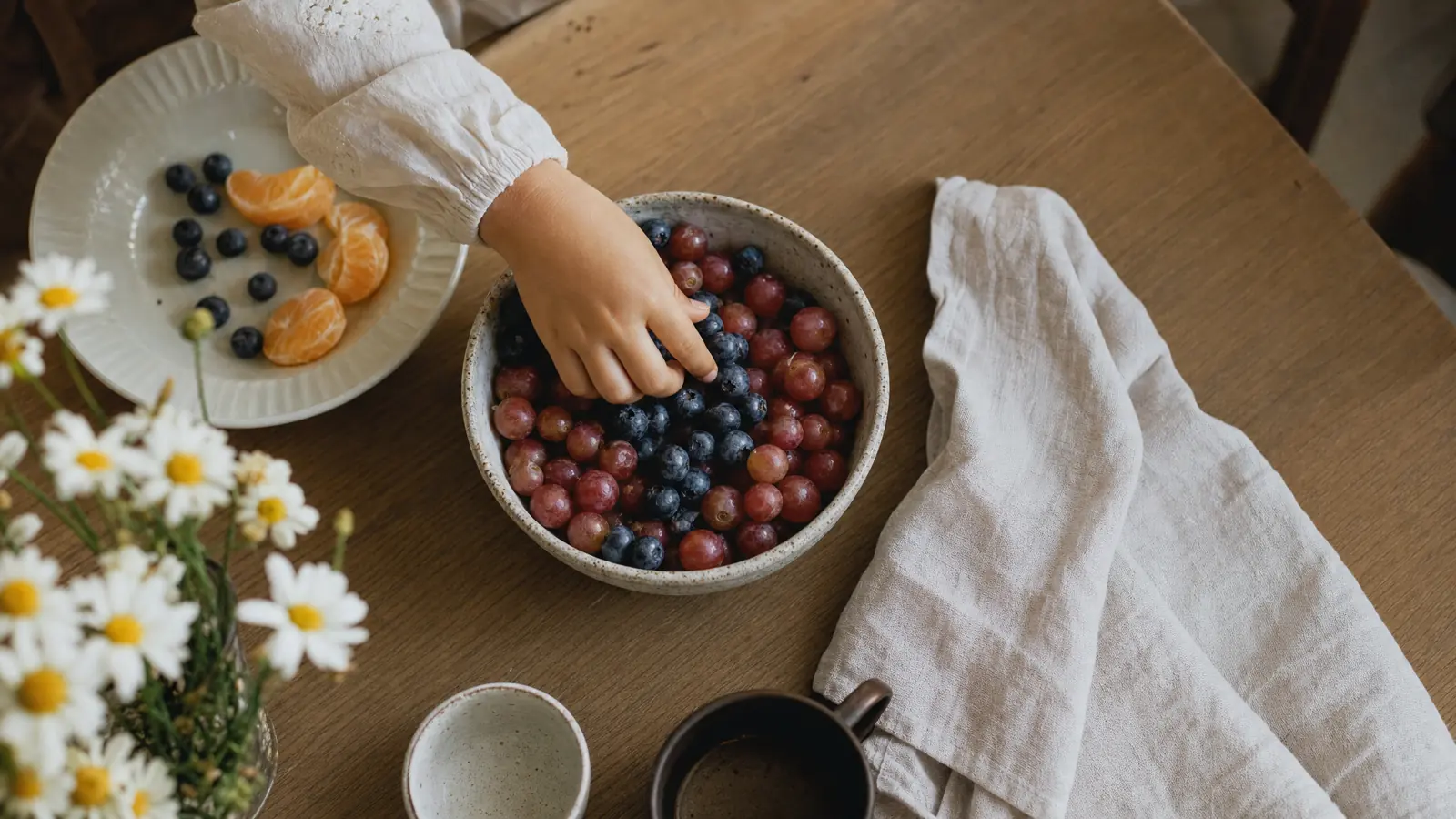 A child's hand reaching into a bowl of blueberries and grapes